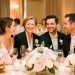 Des invités souriants réunis lors d’une réception de mariage élégante, entourés de tables fleuries dans une lumière dorée et chaleureuse.