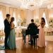 Un jeune couple observe un duo musical près d’une piste de danse dans une élégante salle de réception décorée pour un mariage.